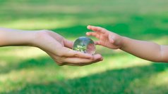 Hand einer Erwachsenen reicht Kinderhand eine Erdkugel